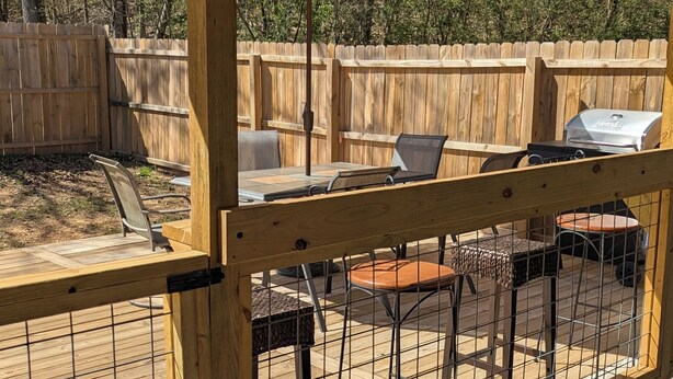Una veranda esterna riparata con pavimento in legno, un tavolo con sedie, un barbecue e un ombrellone grande.