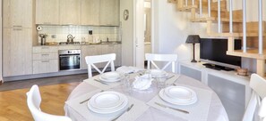 A modern kitchen with white cabinetry, a dining table set for four, and a television in the corner. - THREE-ROOM APARTMENT, SLEEPS 4, SHELL AREA-Rif. Pianosa (San Vincenzo)