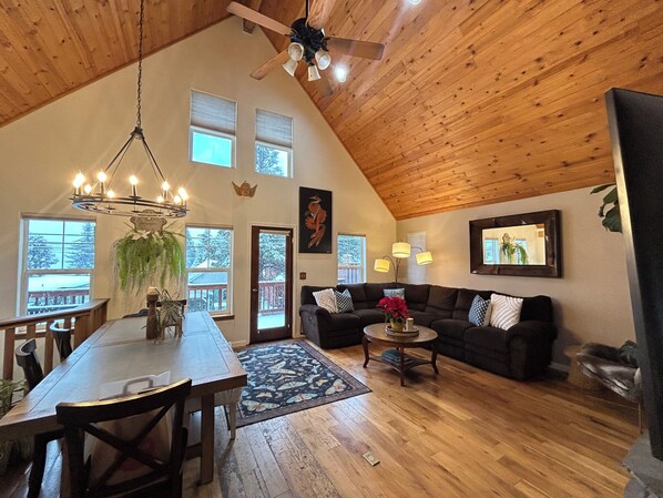 Un loft spacieux avec un plafond haut, des poutres apparentes, un coin repas avec une table et des chaises, un canapé et une petite table basse.