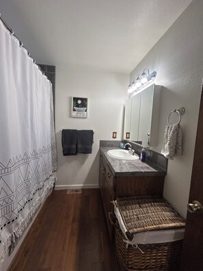 Une salle de bain avec un rideau de douche, un lavabo, un miroir et un panier en osier.
