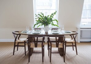 A dining table with six chairs, a potted plant, and a window with blinds. - The Mayfair Grand Penthouse (London)