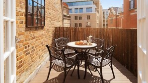 Eine Terrasse mit rundem Tisch und Stühlen, einem Holzzaun und einem Backsteinhaus.