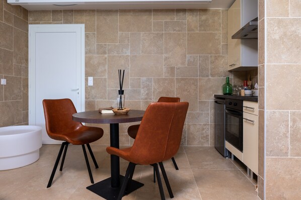 A compact kitchen with a dining area, featuring a round table, two chairs, a white door, and a built-in oven.