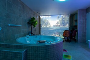 A bathroom with a large bathtub, a shower, and a view of a tropical landscape.