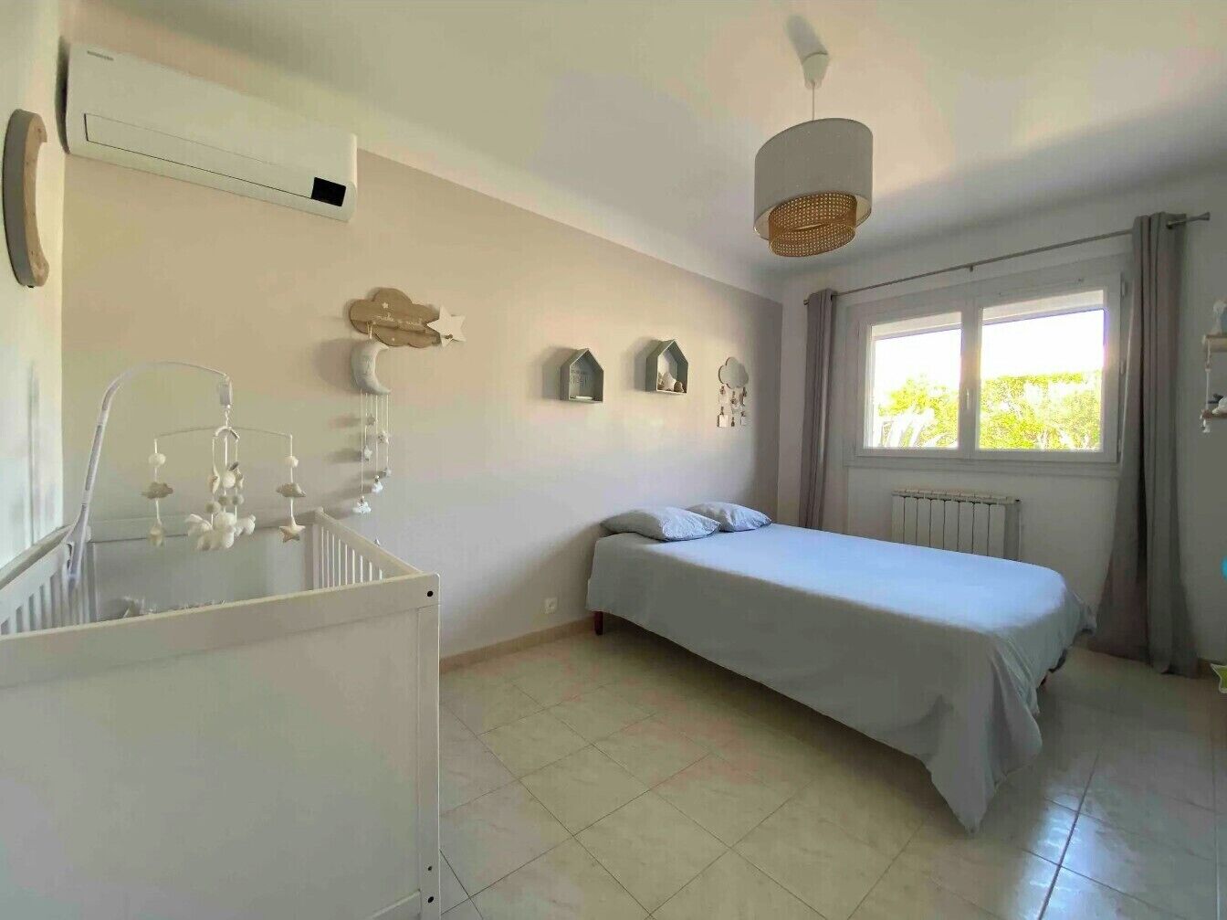 A bedroom with a bed, a radiator, a window with curtains, a hanging light fixture, and a wall-mounted air conditioner.