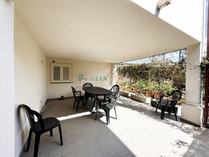 Eine Terrasse mit Tisch und Stühlen, ein Fenster mit Rollläden und eine Wand mit einem Logo.