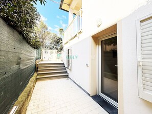 Ein schmaler Gang, der zu einem Gebäude mit einer Schiebeglastür und einem kleinen Balkon führt.