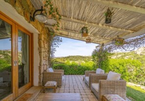 Eine überdachte Terrasse mit Korbmöbeln, Steinwänden und hängenden Pflanzen.