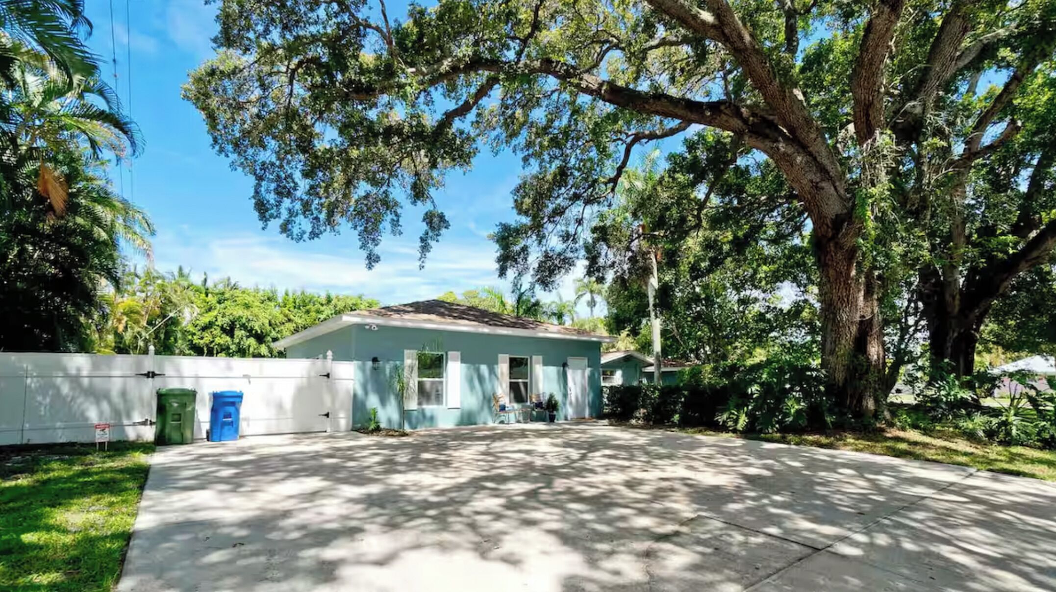 A single-story house with a large tree in front, a clear sky, and a well-maintained lawn.