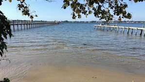 En strand med en träbrygga som sträcker sig ut i stilla vatten, omgiven av träd.