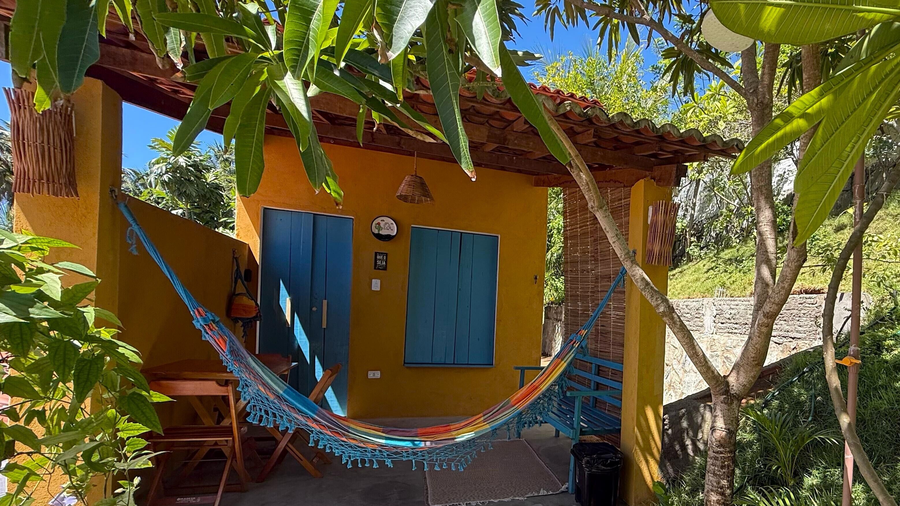 Un edificio giallo con persiane blu, un'amaca e una panchina in legno.