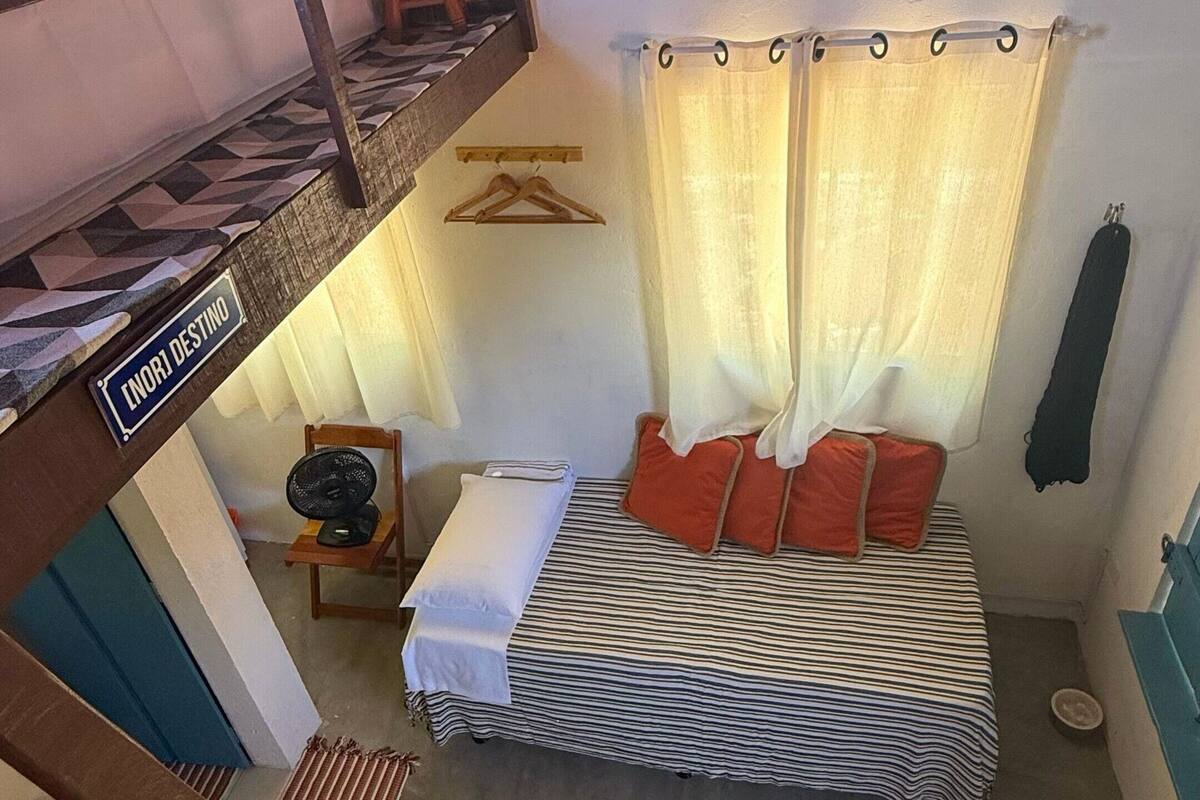 Ein Schlafraum im Studentenwohnheimstil mit einem Etagenbett, einem Einzelbett mit gestreifter Bettwäsche, einem kleinen Tisch mit Ventilator und einem hängenden Korb.