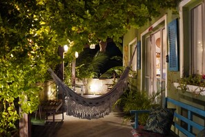 Μια αιώρα σε έναν καλά φωτισμένο εξωτερικό χώρο, με φυτά και ένα παγκάκι.