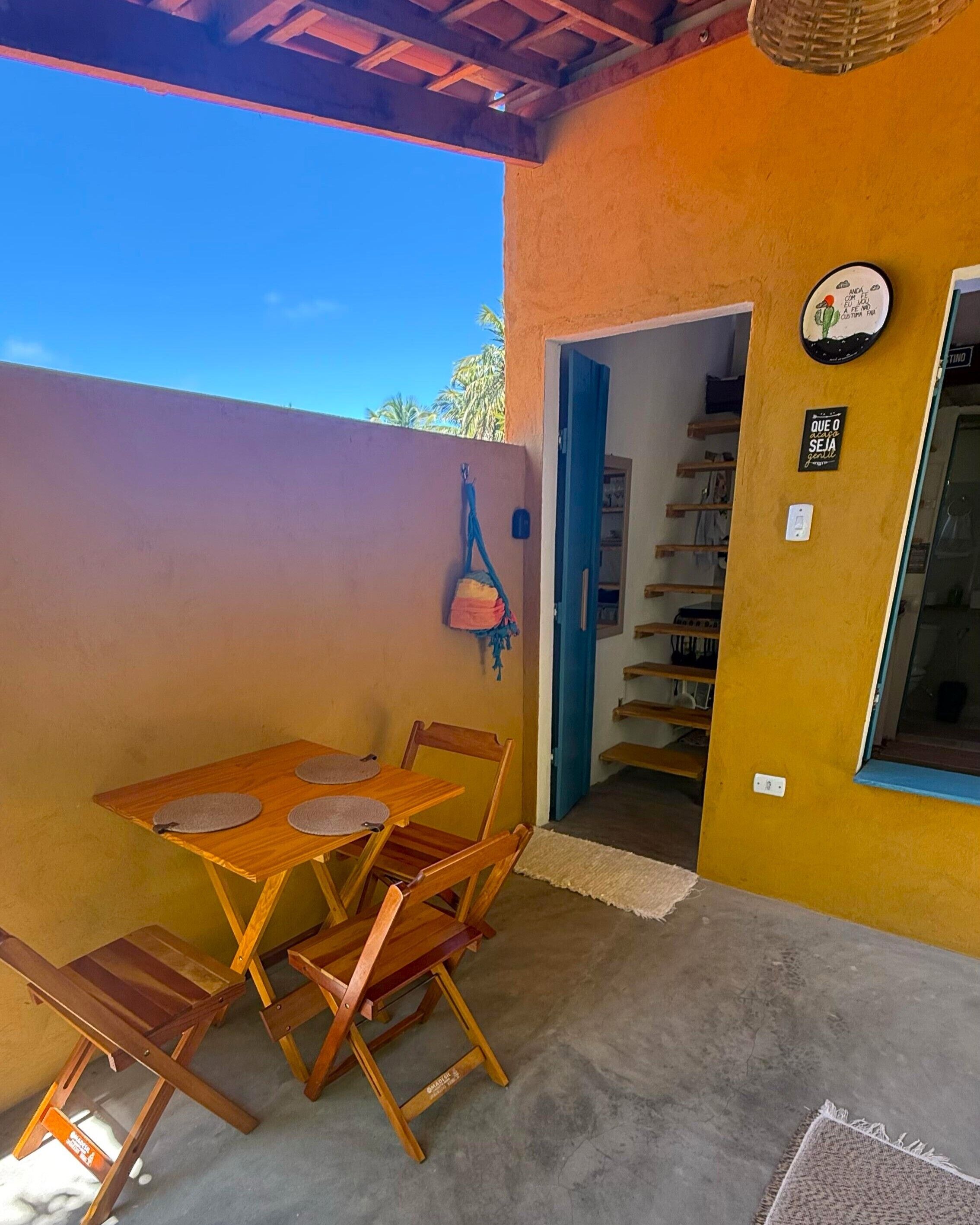 Un patio con una mesa y sillas, un bolso colgado, un reloj de pared y una puerta que da a un espacio interior.