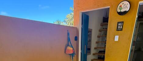 Un patio con una mesa y sillas, un bolso colgado, un reloj de pared y una puerta que da a un espacio interior.