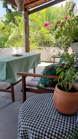 Un área de estar al aire libre con mantel a cuadros, un banco de madera, un taburete estampado de pata de gallo y una planta en maceta.