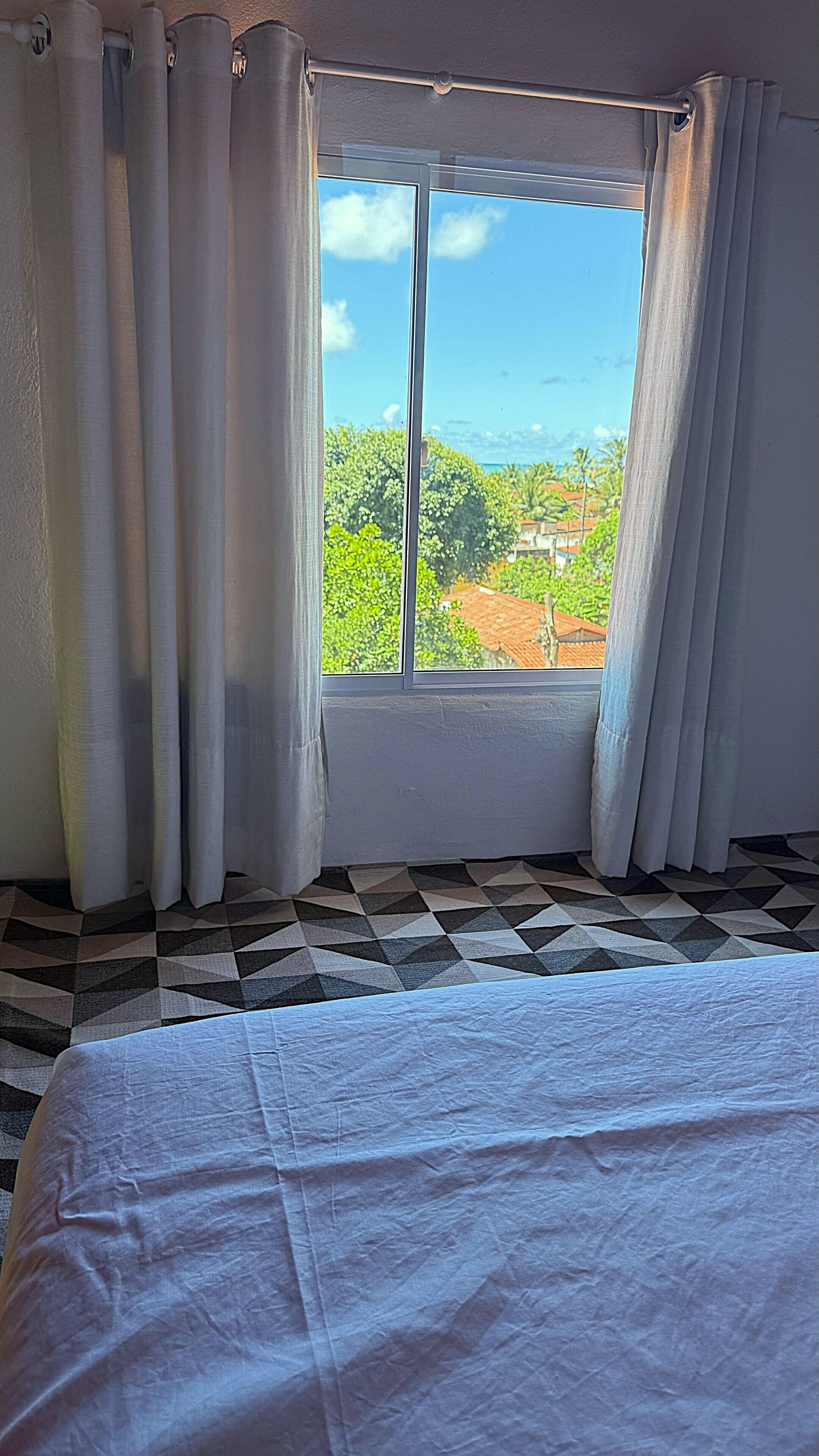 A room with a large window, a bed, and a checkered floor.