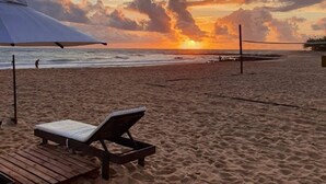 Ein Strand mit Sonnenuntergang, Volleyballnetz und Liegestühlen.