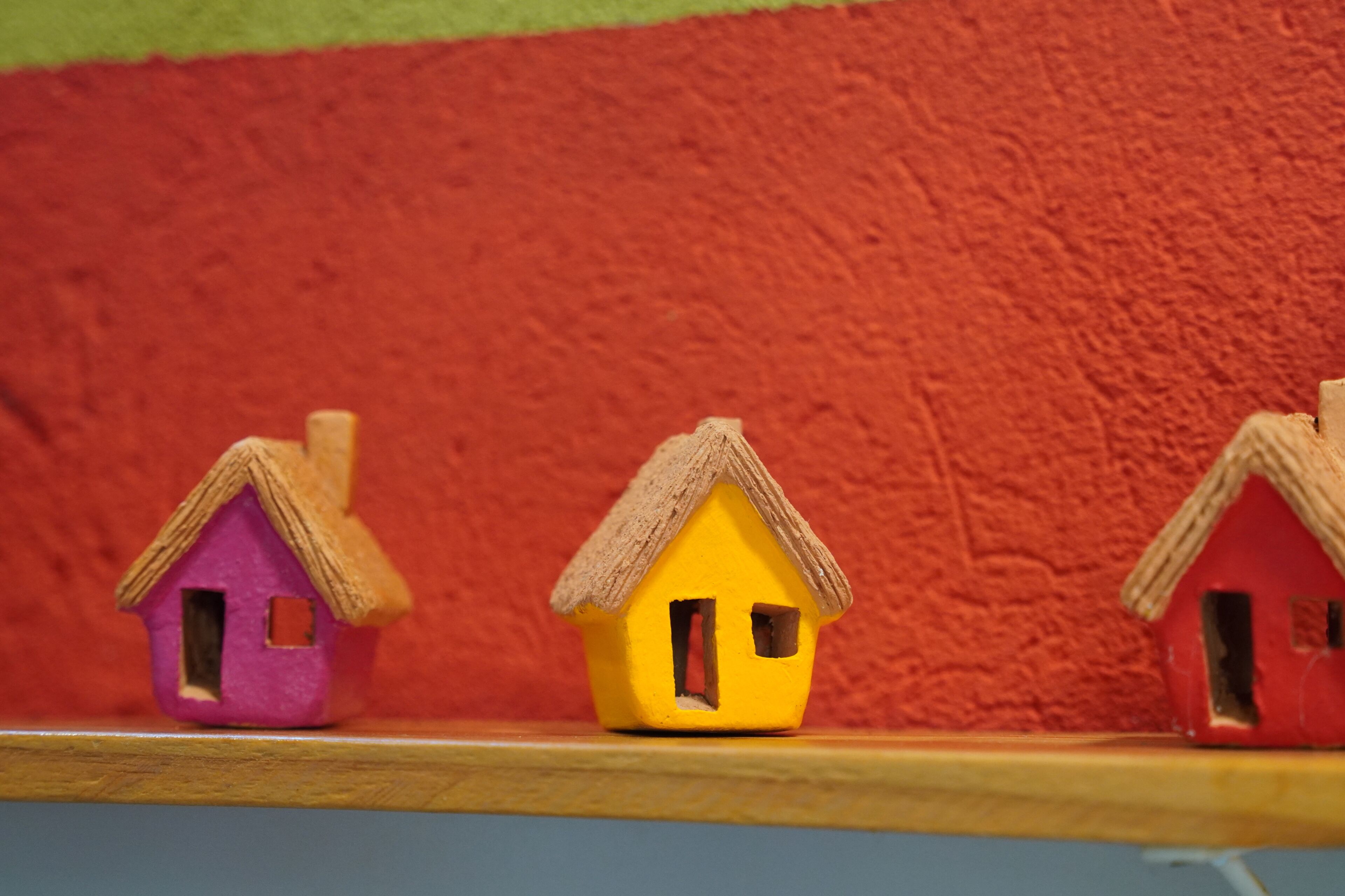 Three small houses on a shelf against a textured wall.