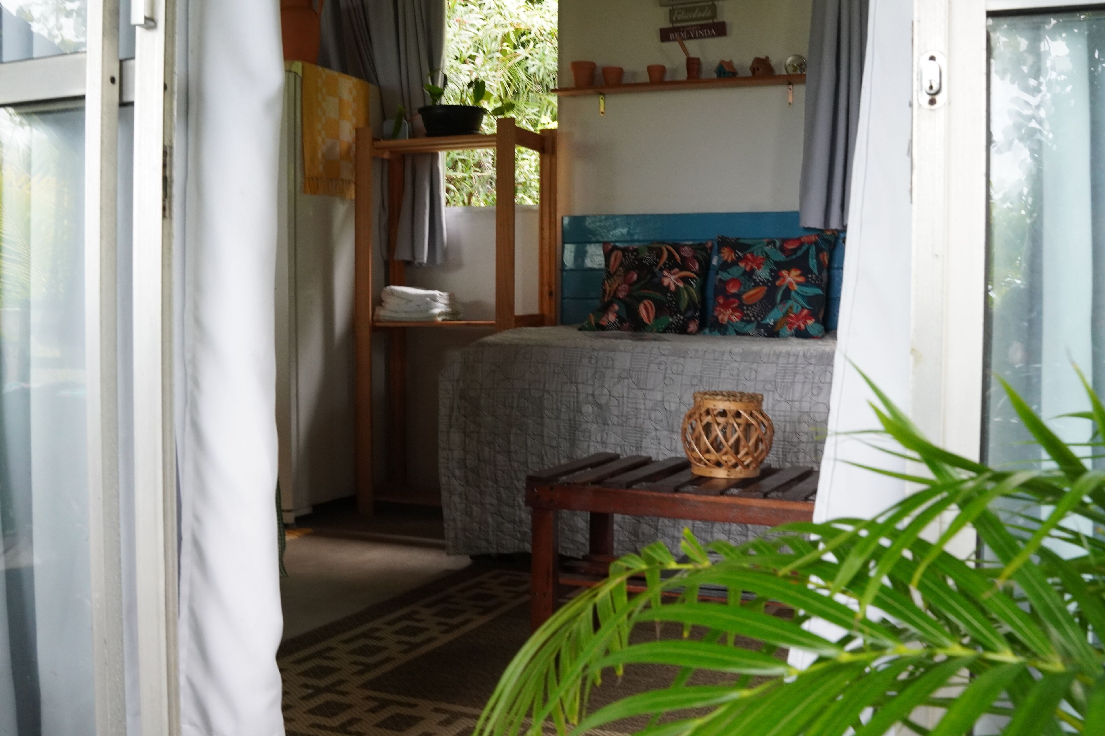 A room with a bed, a wooden bench, a shelf with folded towels, and a potted plant.