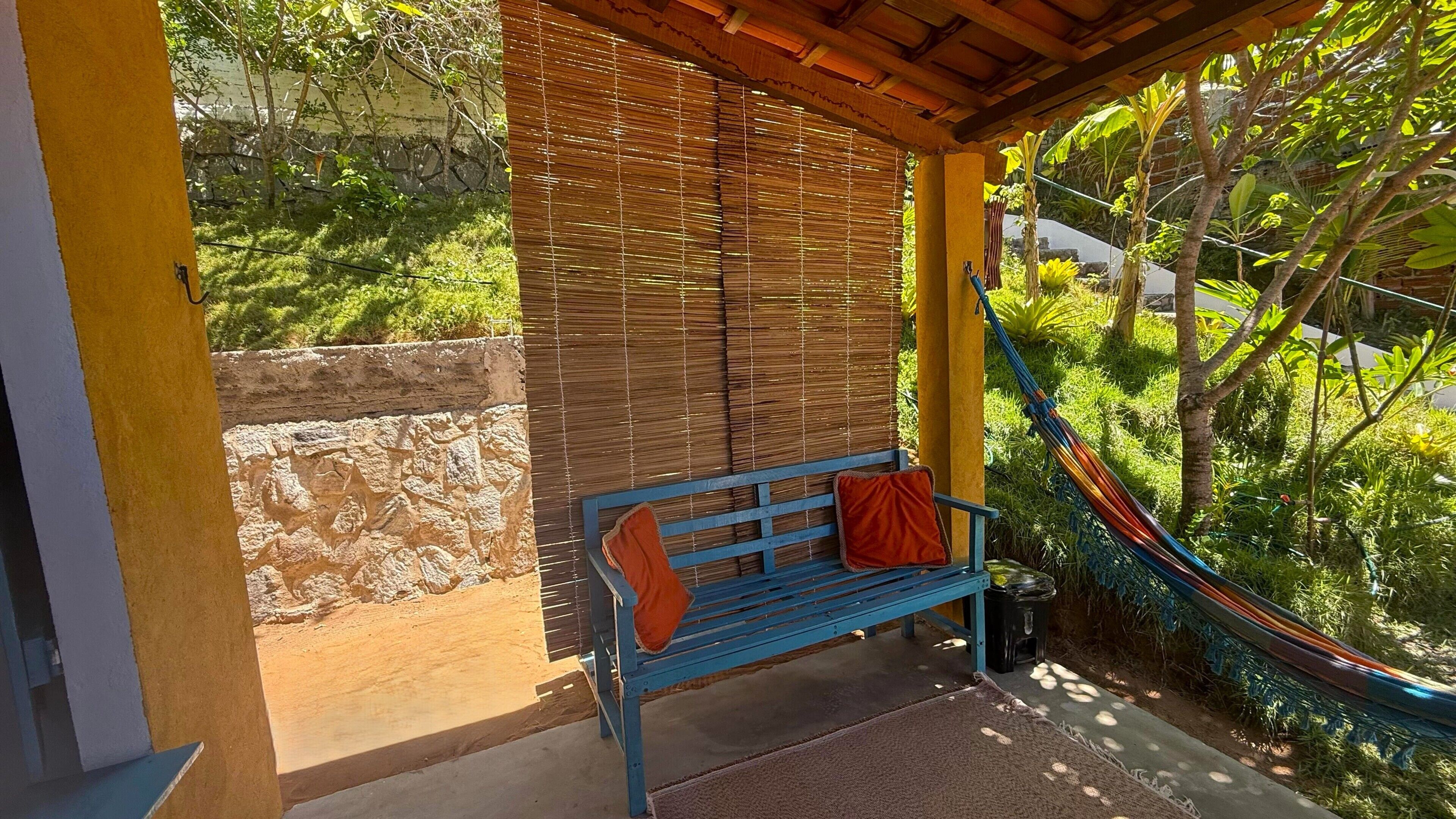 Un banco azul con cojines anaranjados, una hamaca y un muro de piedra.