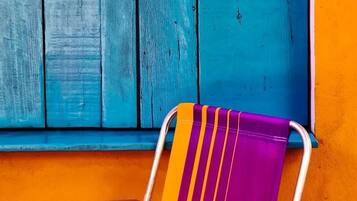 Una silla con respaldo a rayas y estructura metálica, ubicada frente a una ventana con contraventanas de madera azul.