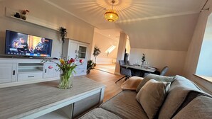 A modern living room with a flat-screen TV, a sofa, a dining table, and a chandelier. - To Huus modern apartment with country view near Verden (Verden (Aller))