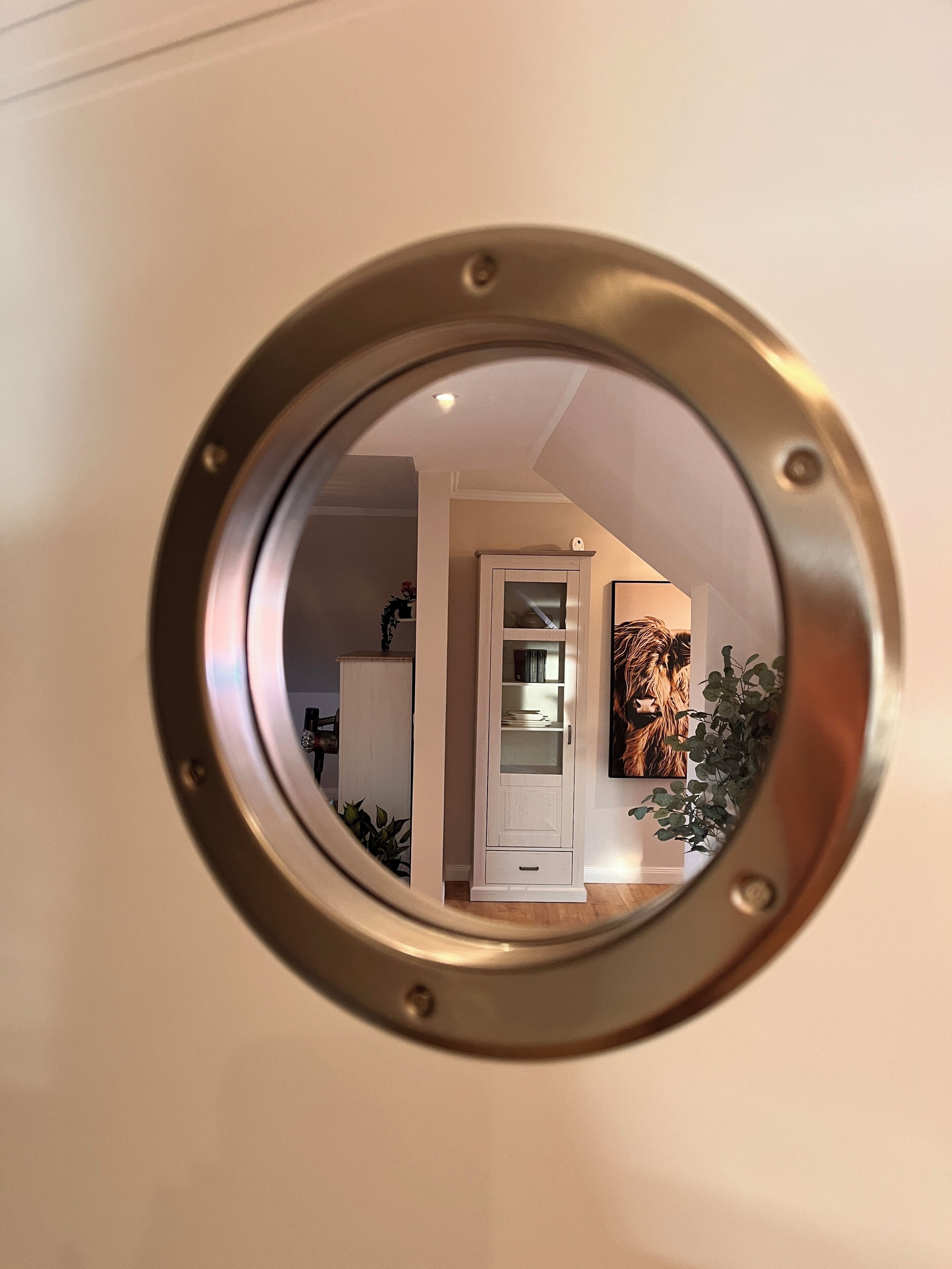 Un miroir rond doté d’un cadre métallique, qui reflète l’intérieur d’une pièce.