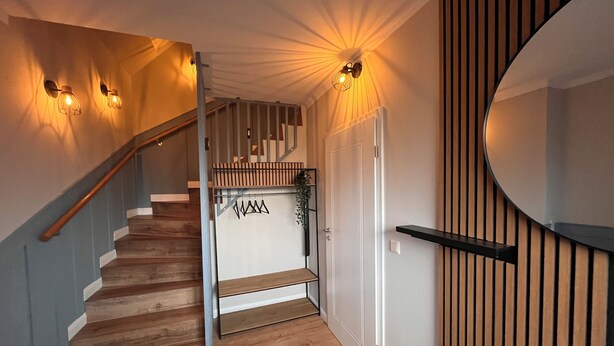 A wooden staircase with a handrail, a white door, and a wall-mounted mirror. - To Huus modern apartment with country view near Verden (Verden (Aller))