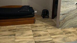 Habitació amb un llit, un televisor fixat a la paret, un petit tamboret i un mur amb disseny de marbre.