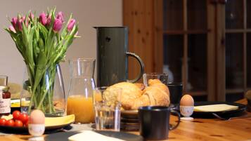 Ett frukostbord med en vas med blommor, en kanna, ett glas apelsinjuice, en croissant och en kopp.