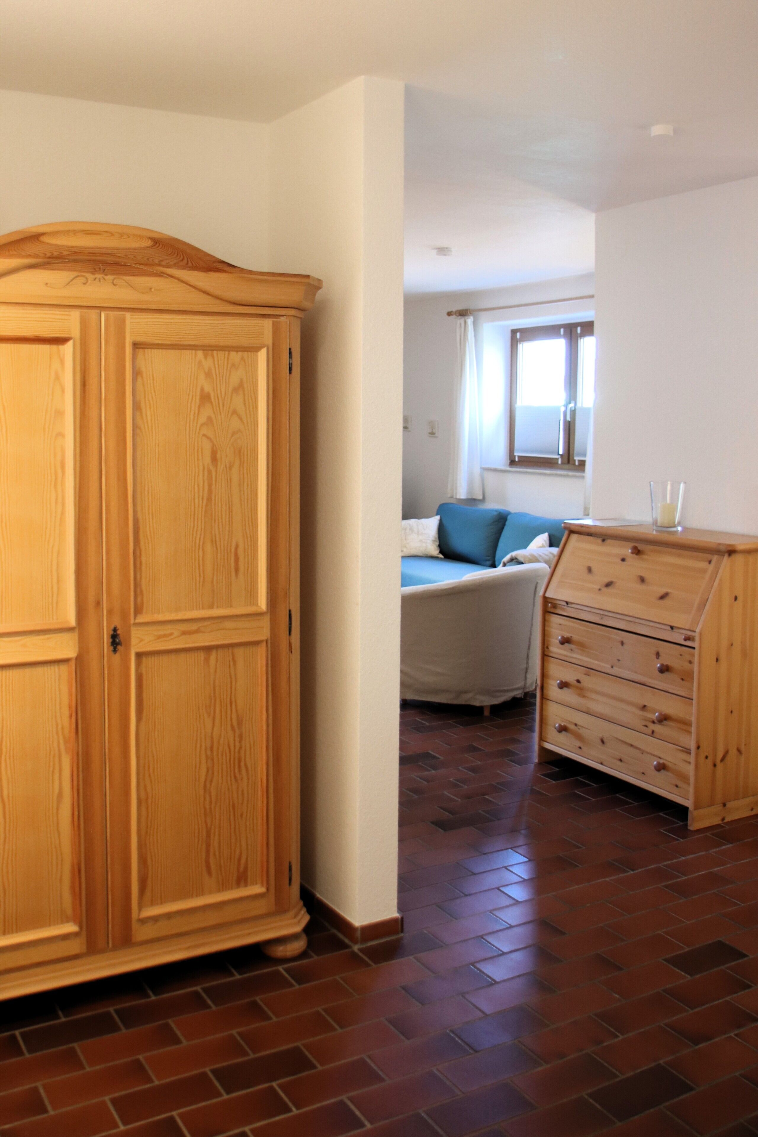 Una habitación con un armario grande de madera, una cama con cabecera azul y un aparador con cajones.
