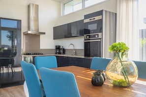 Une cuisine moderne avec des meubles noirs, des appareils en acier inoxydable et un coin repas doté de chaises bleues et d’une table en bois.