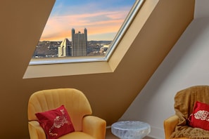 Ein Zimmer mit einem Oberlicht, zwei Stühlen und Blick auf eine Stadtlandschaft.