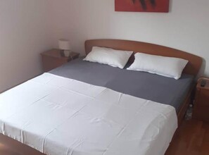 Un lit bien fait, avec une literie blanche et grise, une tête de lit en bois et une petite table de chevet avec une lampe.