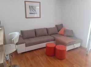 Un salon moderne avec un canapé d’angle, un fauteuil blanc et deux poufs rouges.