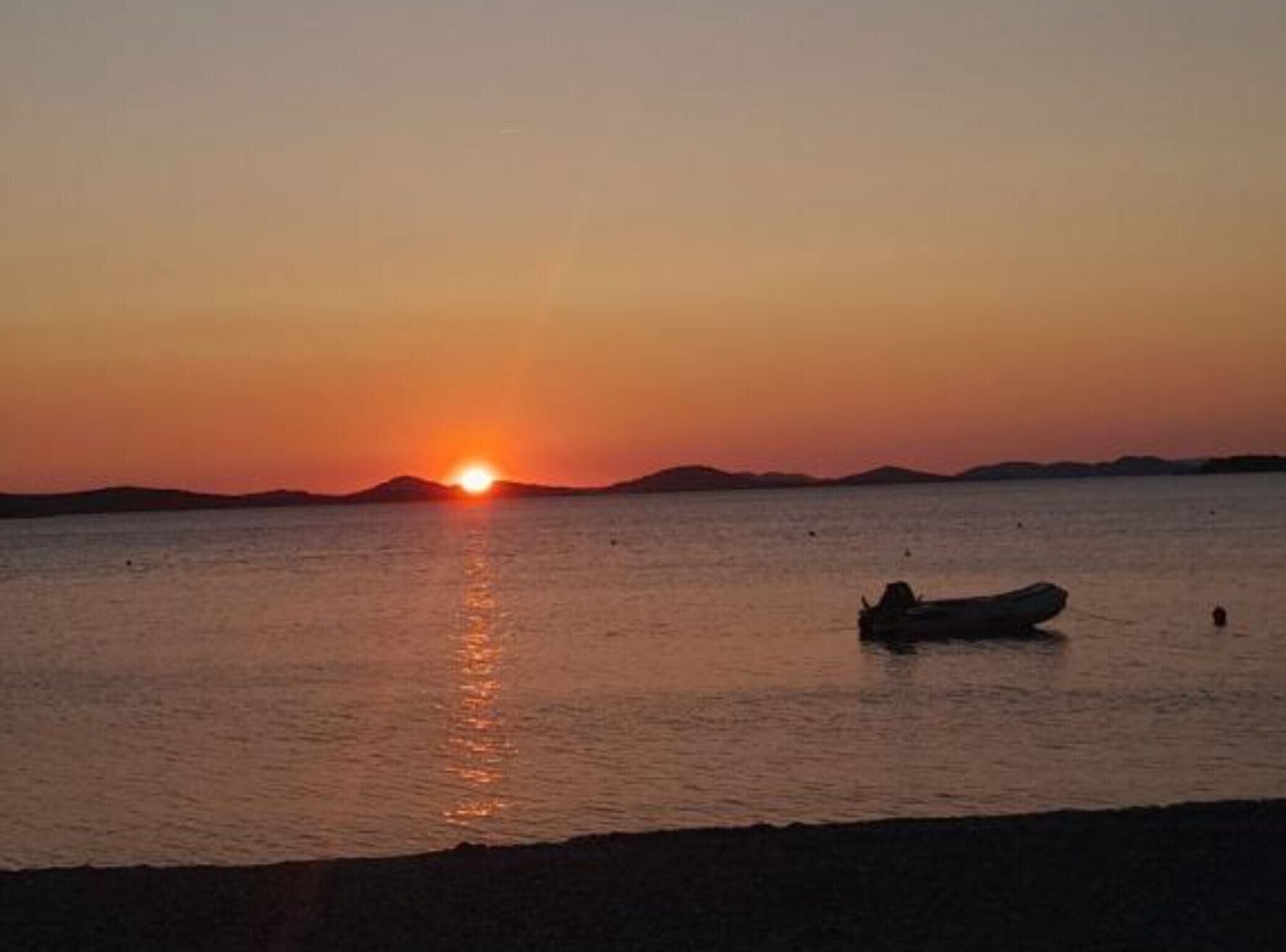 A sunset over a calm sea with a boat in the foreground.