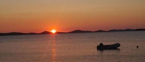 A sunset over a calm sea with a boat in the foreground.