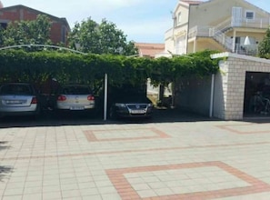 A parking area with three cars, a building with a balcony, and a small brick structure. - Villa Ivan Vodice -Studio Apartment with Balcony 3 (Vodice)