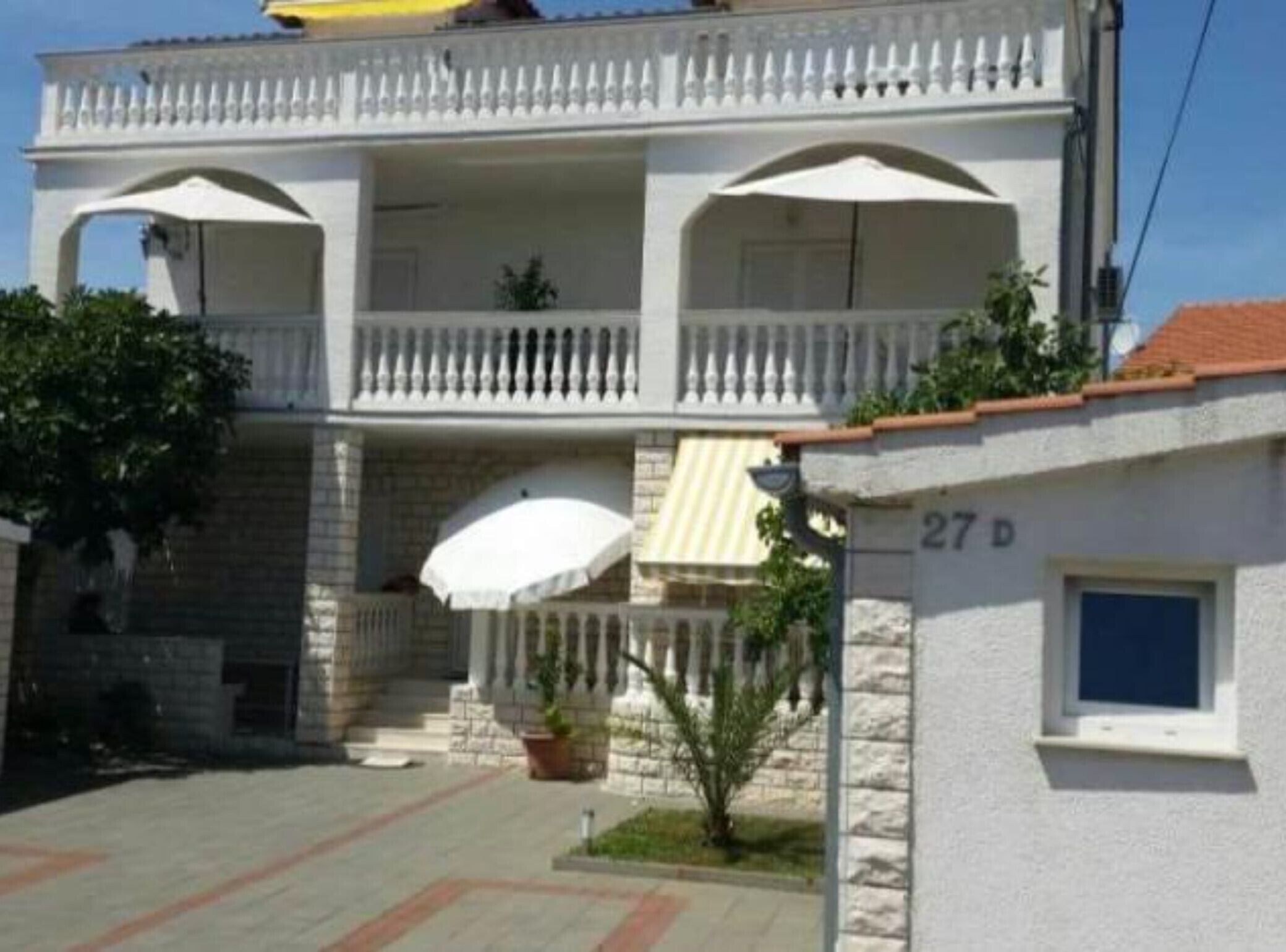 A two-story building with a balcony, a small garden area, and a visible door number.