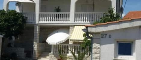 A two-story building with a balcony, a small garden area, and a visible door number.