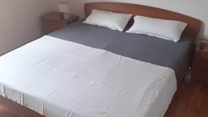 Een enkel bed met een houten hoofdbord, een nachtkastje met een lamp, en een rode afbeelding aan de muur.