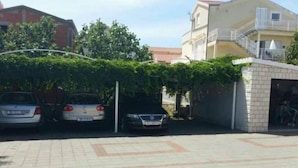 Een parkeerplaats met drie auto's, een gebouw met een balkon en een klein bakstenen gebouwtje.