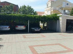 A parking area with three cars, a building with a balcony, and a small brick structure. - Villa Ivan Vodice -Studio Apartment with Balcony 4 (Vodice)