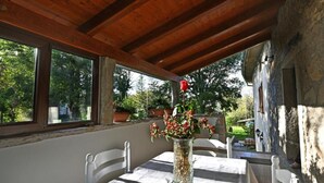 Ein Essbereich im Freien mit Tisch und Stühlen, einer Holzbalkendecke und Blick ins Grüne.