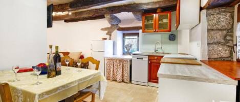 Cocina rústica con vigas a la vista, comedor con mesa para dos y pared de piedra.