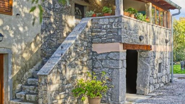 Ein Steinhaus mit einer Holztreppe, die zu einer Veranda mit Blumentöpfen führt.