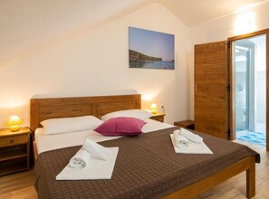 Un dormitorio con cama de madera, mesita de noche, lámpara, ventana con vistas y puerta corrediza que da a un baño.