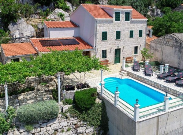 Una villa con piscina, paredes de piedra y tejado de tejas rojas.