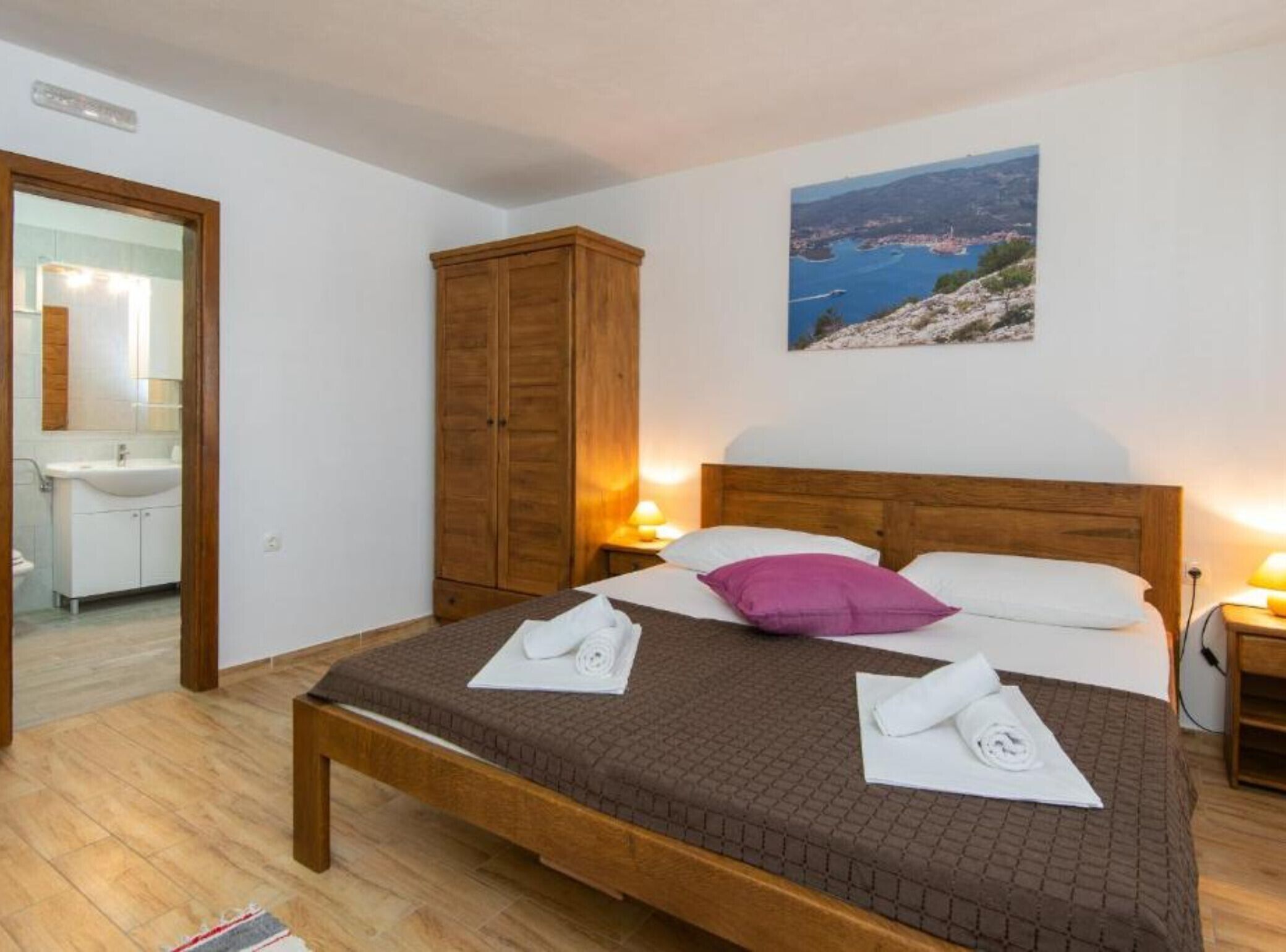Una camera da letto con un letto di legno, un comodino con una lampada, un armadio e un bagno visibile sullo sfondo.